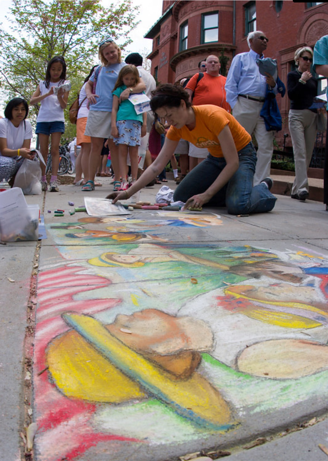 Dana Ellyn kneeling on the sidewalk outside The Phillips Collection, working in pastel chalk on a large-scale recreation of Renoir's Luncheon of the Boating Party, with a crowd gathered behind her